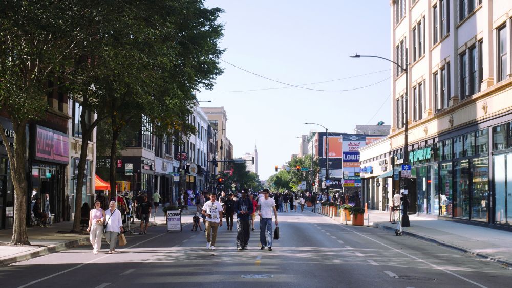 Pedestrians walk down the middle of Milwaukee Avenue, surround be small shops and no parked cars.