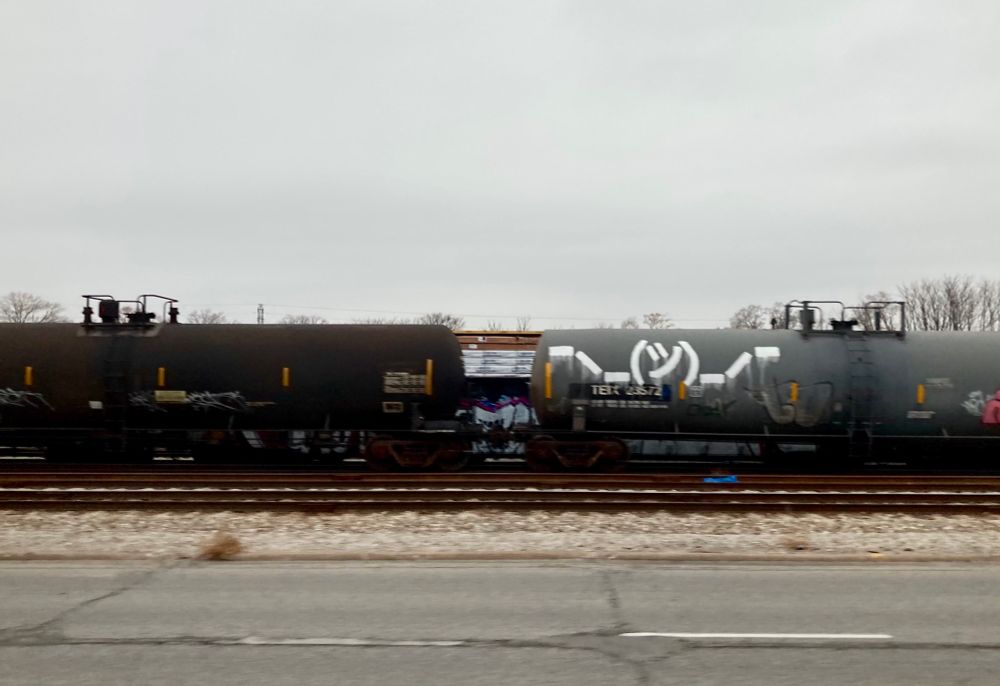 A tanker train car with shrug emoji graffiti.