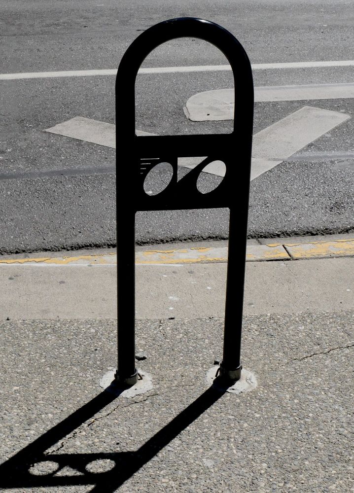 A bike rack with a simple geometric symbol inlaid: a bike made of two circles and a V-shaped triangle and some speed lines.
