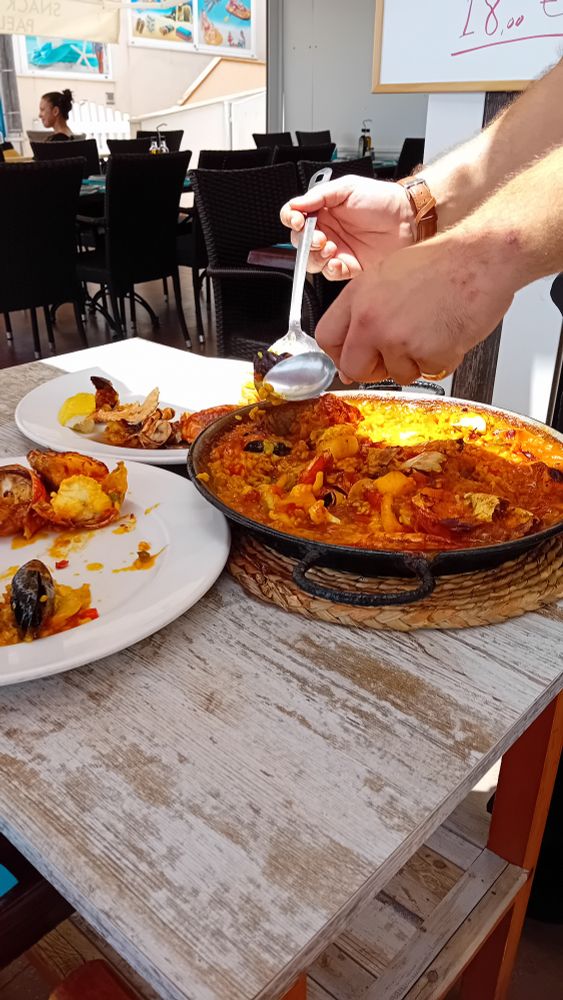 Paella being plated from a pan at the table.