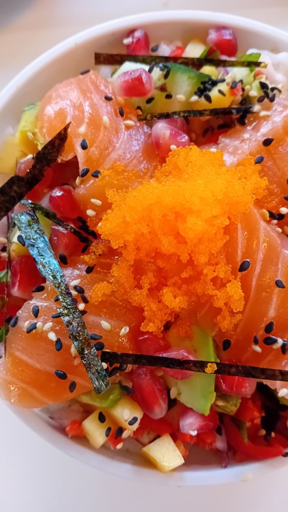 Close-up up view of a very vibrant poke bowl with salmon, mango salsa and fish eggs. The dominant colours are Red and orange. Everything looks very fresh and appetising. 