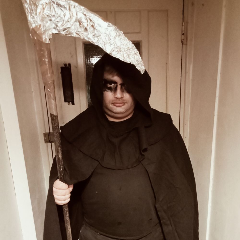 me dressed as the grim reaper in a black hooded cloak and holding a scythe 