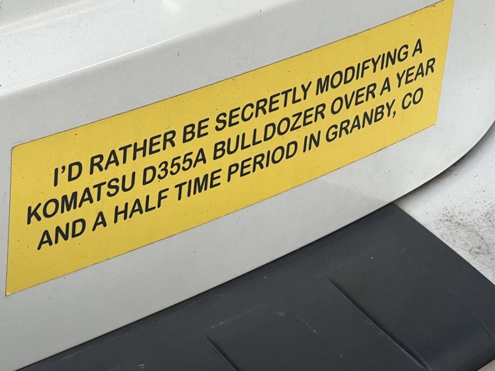 Bumper sticker that reads: I'D RATHER BE SECRETLY MODIFYING A KOMATSU D355A BULLDOZER OVER A YEAR AND A HALF TIME PERIOD IN GRANBY, CO