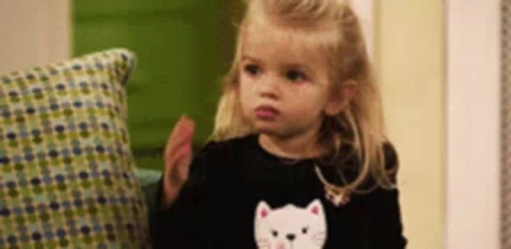 a little girl wearing a black sweater with a cat on it is clapping her hands .