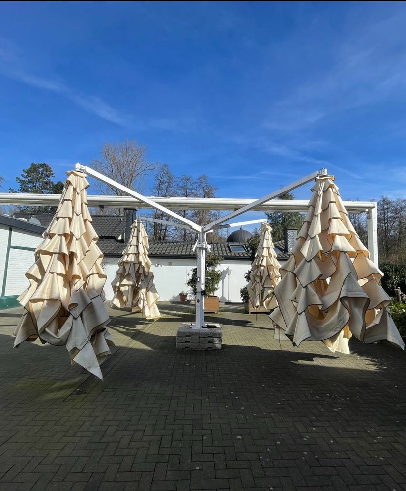 Vier weiße oich geschlossene Schirme in einem gepflasterten, unmöblierten Biergarten 