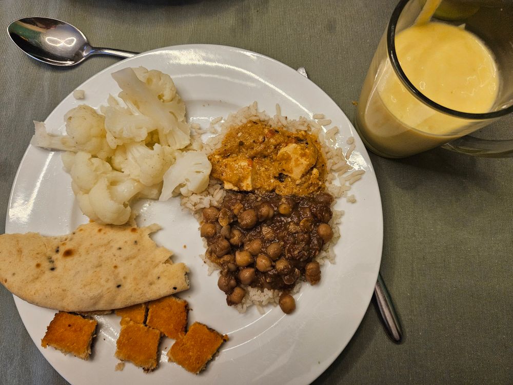 Rommelig bord met reeds genoemde gerechten op een rijstbedje; de mangodrink staat ernaast
