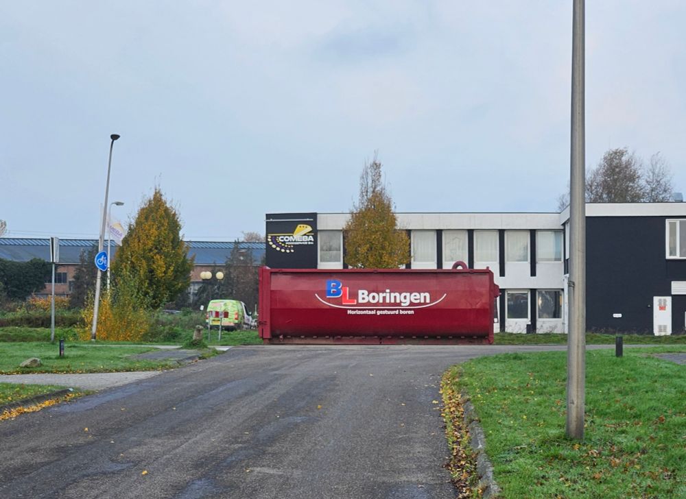Grote rode cilindervormige container met opschrift 'Boringen' waar de straat bij een kanaal uitkomt