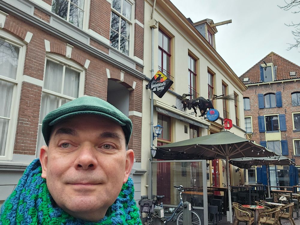 Man met groene et een möbius col voor bierencafé De Heks, compleet met heks op bezemsteel