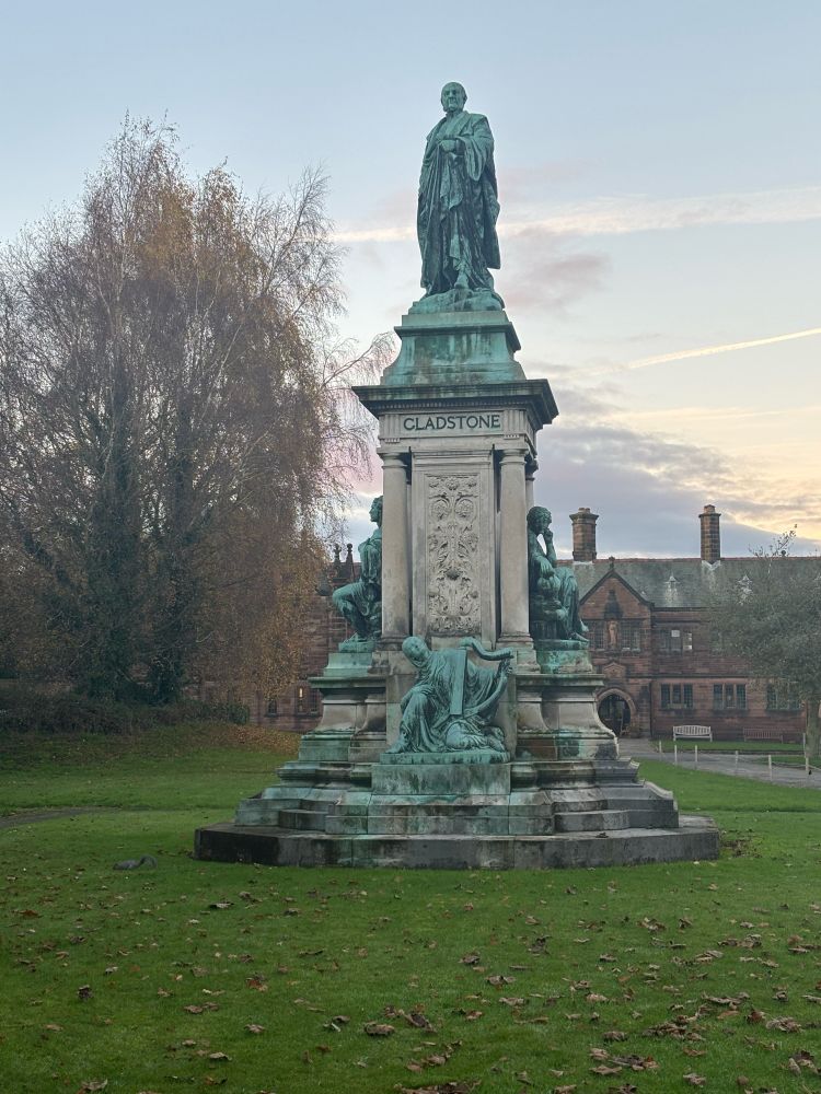 An ornate statue of Gladstone, set on a green lawn, with Gladstone’s Library in the background. 