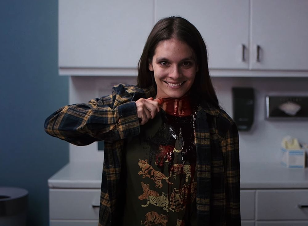 A young woman cutting her own throat with a piece of broken pottery, smiling with unsettling intensity.