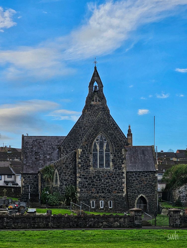 A church surrounded by a graveyard, with blue skies above and behind the church .