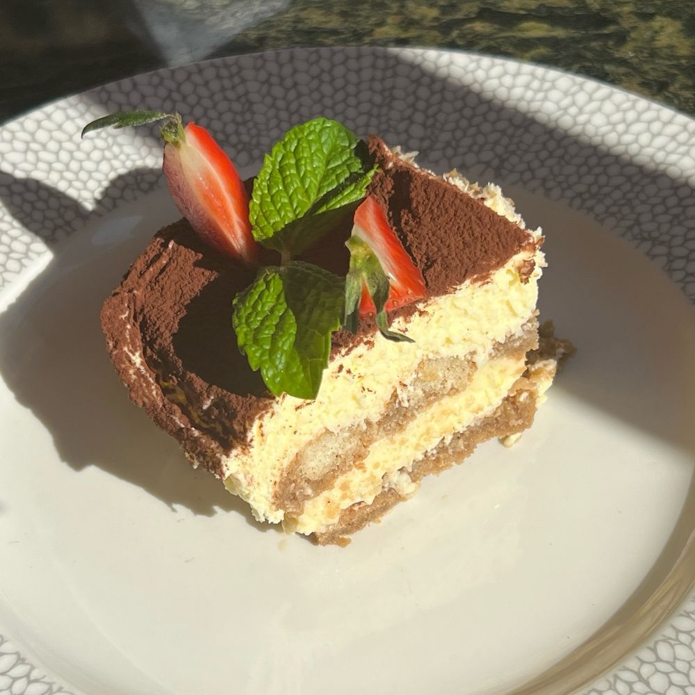 a nice slice of tiramisu topped with strawberry slices and a sprig of mint on a white plate