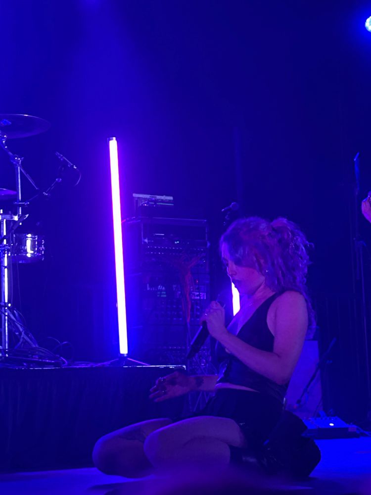 woman knelt on stage singing into a microphone