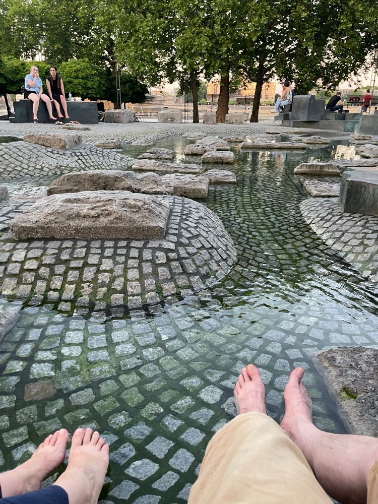 Two sets of feet resting in a cobbled water feature 