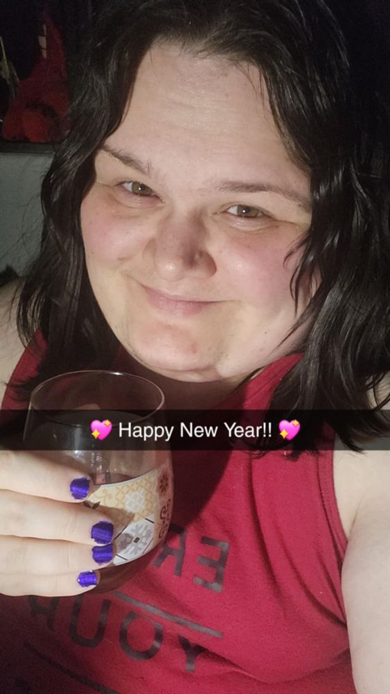 Picture of a girl in a red shirt, holding a wine glass with purple nails, and brown, medium length hair with a caption that reads Happy New Year!!
