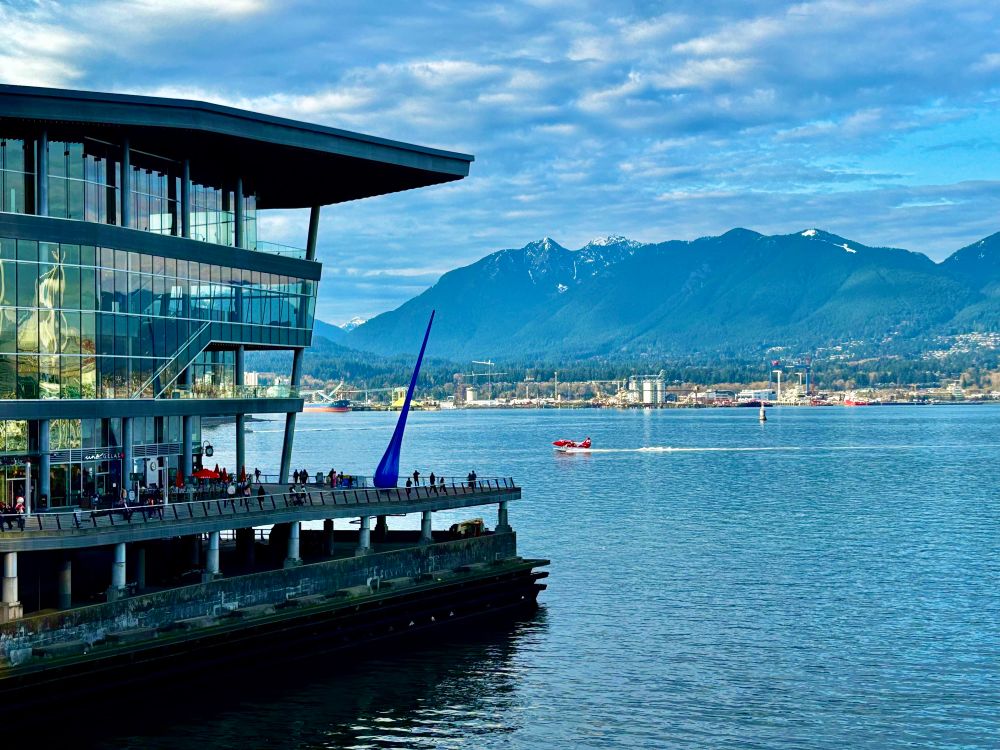 Photo of a red seaplane landing in the harbour behind the Vancouver Convention Center where the TED conference center. 