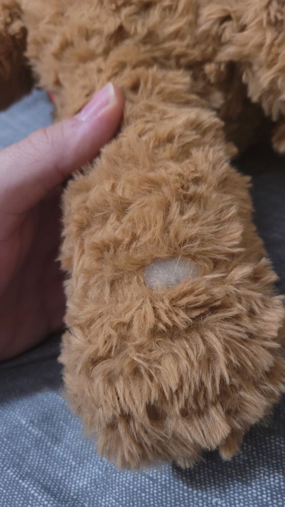 A small hole on the seam between a plush dog's leg and foot.