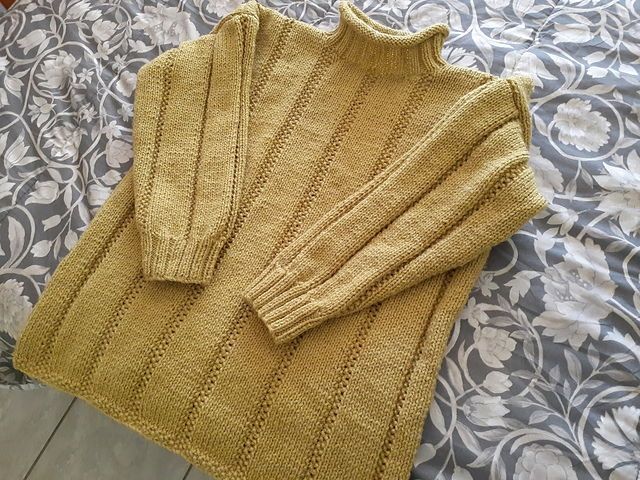 A photo of a knitted mustard sweater on a bed with a floral print comforter. 