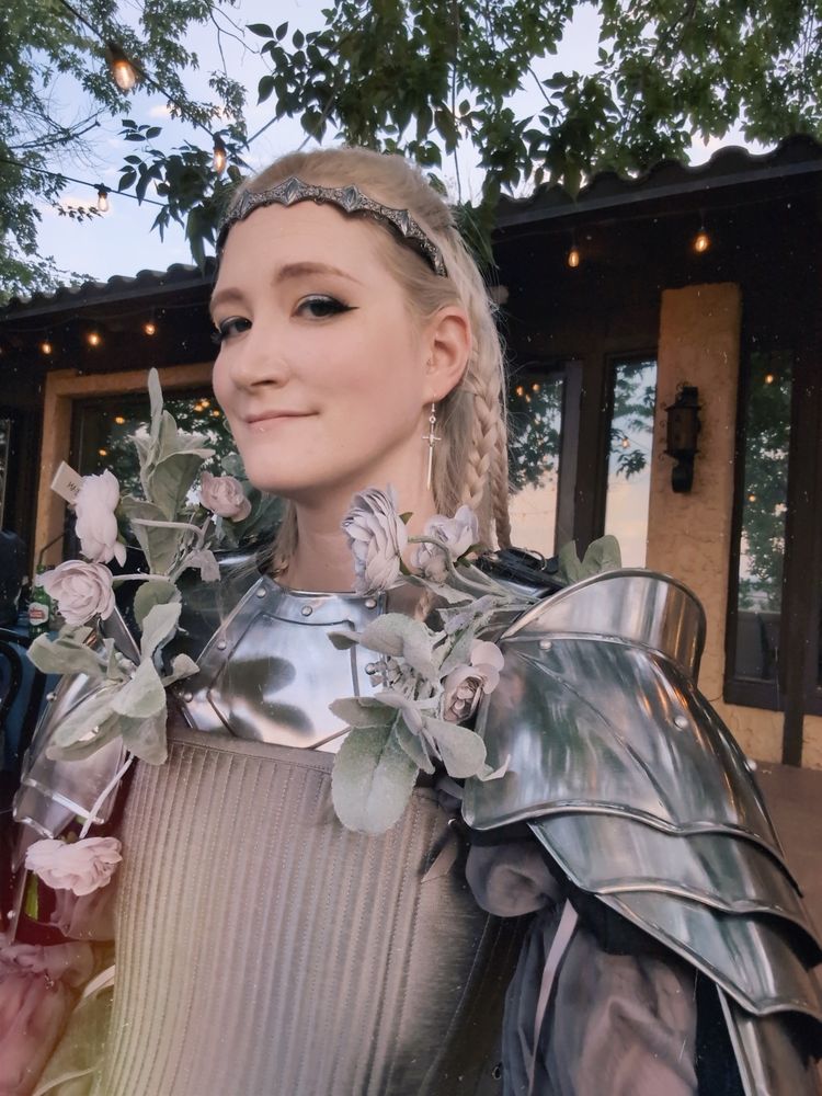 A female knight with plate armor, silver stays, silver hair, a silver tiara, and many silk flowers. 