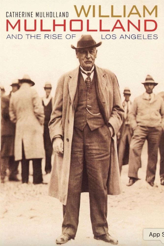 The sepia-colored cover of Catherine Mulholland's book "William Mulholland and the Rise of Los Angeles" shows an elderly William Mulholland standing in front of a number of men as he stares into the camera. 