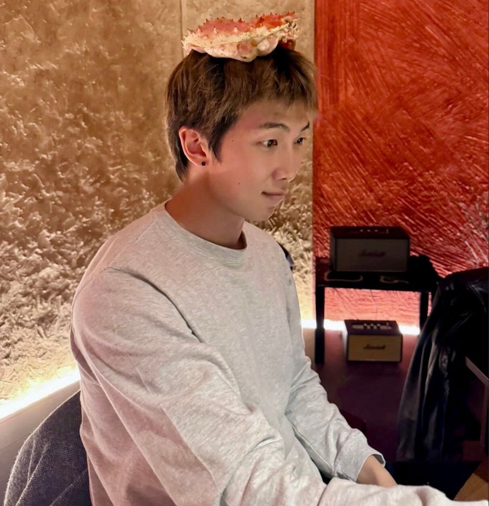 a photo of namjoon in a light gray longsleeve shirt with a large (dead) crab on his head like a hat. 