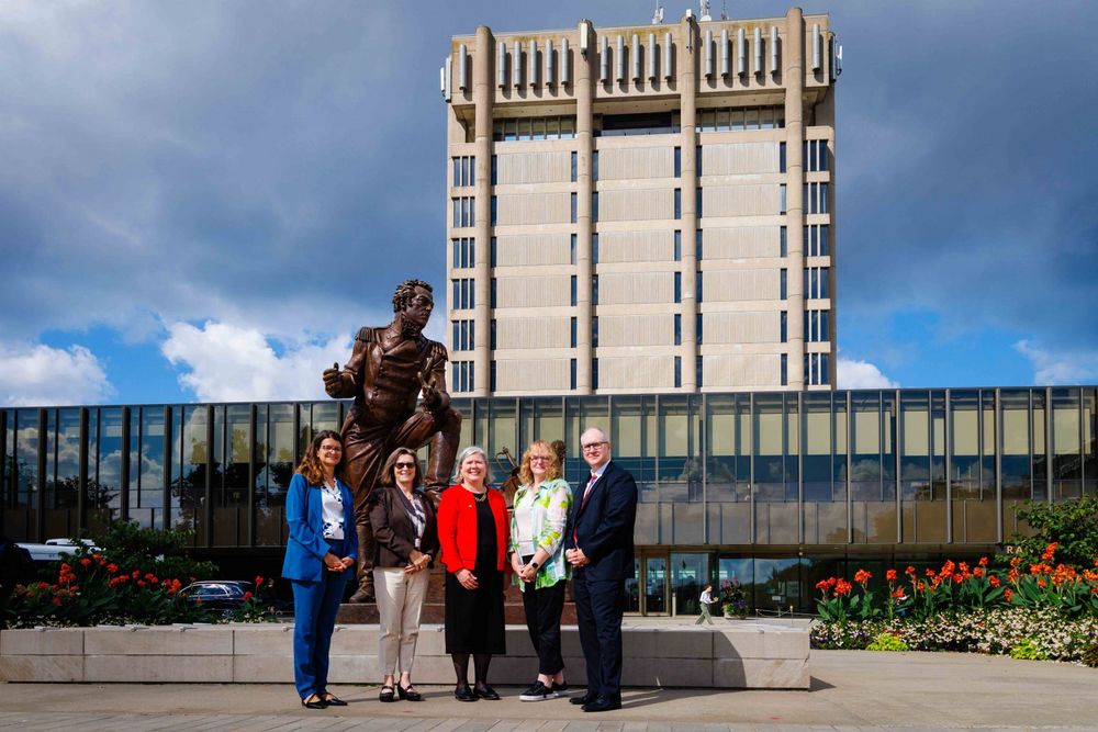 Five people pose in front of a statue and the Schmon Tower at Brock University.