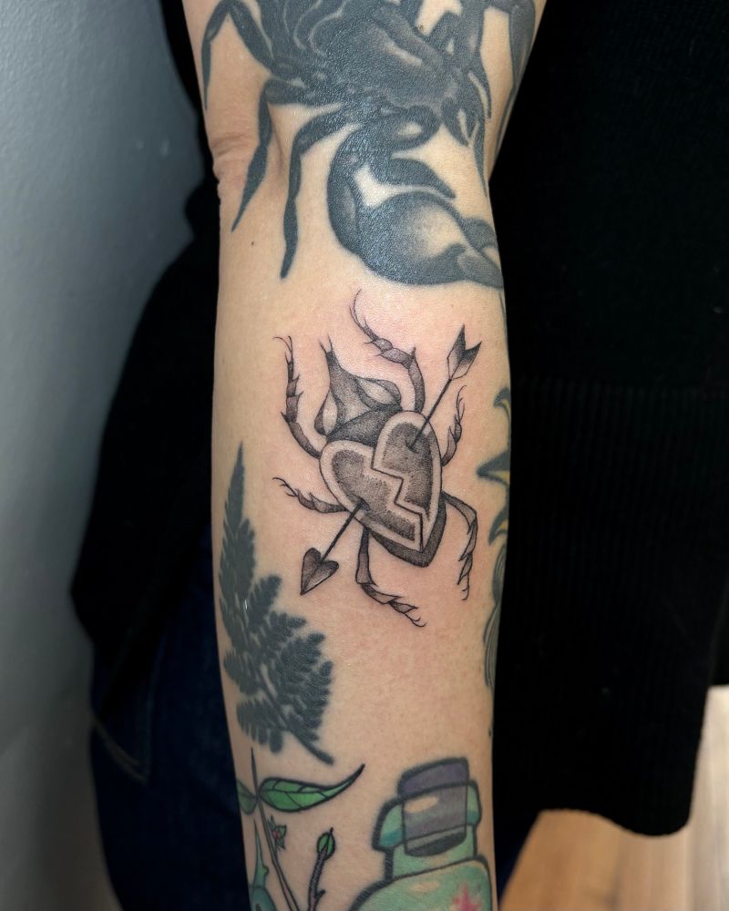 An image of a scarab beetle tattoo, the beetle is heart shaped with an arrow through it 