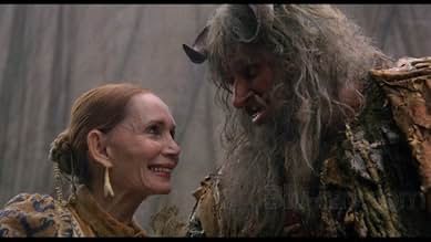 A closeup of a middle-aged red-headed smiling woman with her hair in a bun leaning into a tall unkempt man with long scraggly hair and small curved horns protruding from his forehead. They look like they enjoy each other other’s company.