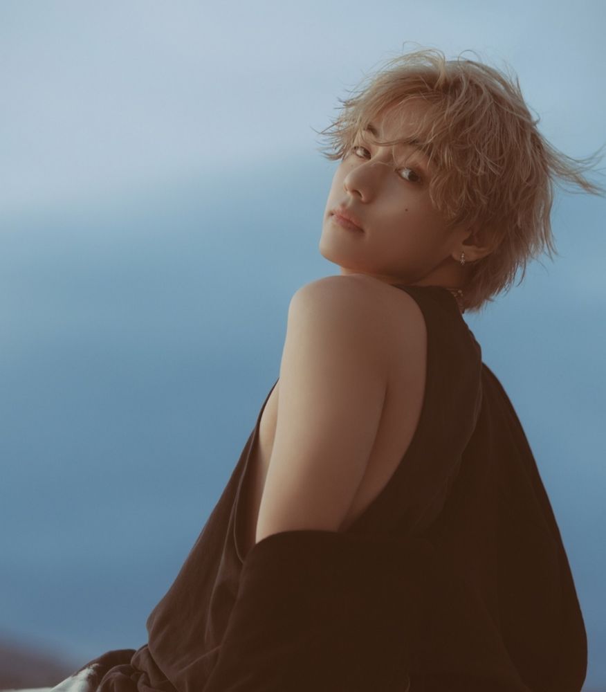 Taehyung circa Layover promotions, his blond hair damp and tousled and beachy. He has a dark sweater falling off of one shoulder that is exposed coquettishly, a dark tank scooping below it. 