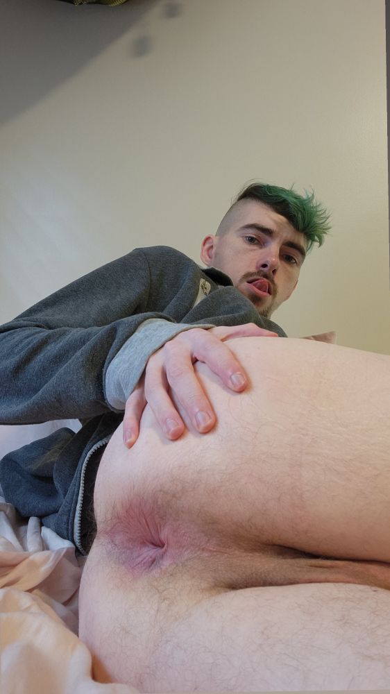 In the same space and outfit as before, I'm now on my side, a hand cupping my butt and pulling it to the side to show off my hole. Again, my tongue is out and flipped against my upper lip with effort. 