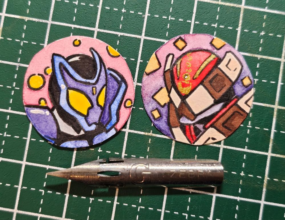 a picture of two small circular watercolor portraits of Kamen Riders Gavv and Valen. they are displayed next to a Zebra G Nib for scale, only being less than about two centimeters or so in size.