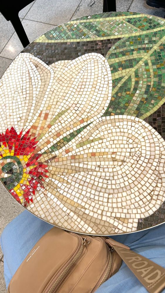 An overhead shot of a small round table covered in a full mosaic of a white flower with a red centre and dark green leaves