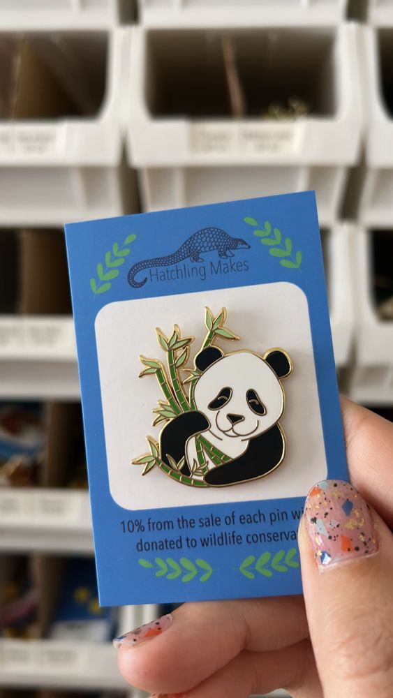 A hand holding an enamel pin of a giant panda on a blue and white backing card