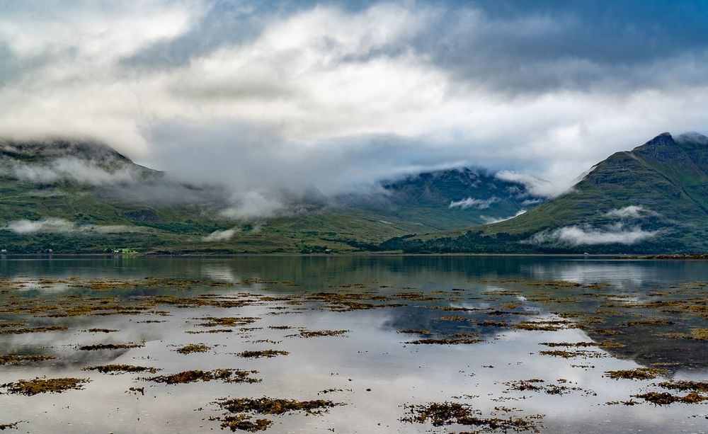 Low cloud over a still sea and mountains.