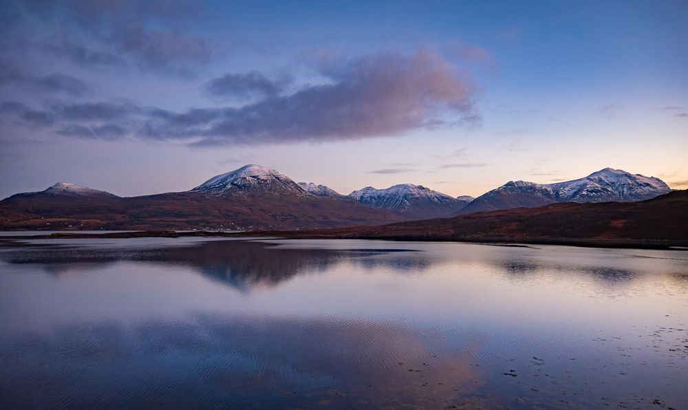 A still sea and snow capped mountains.