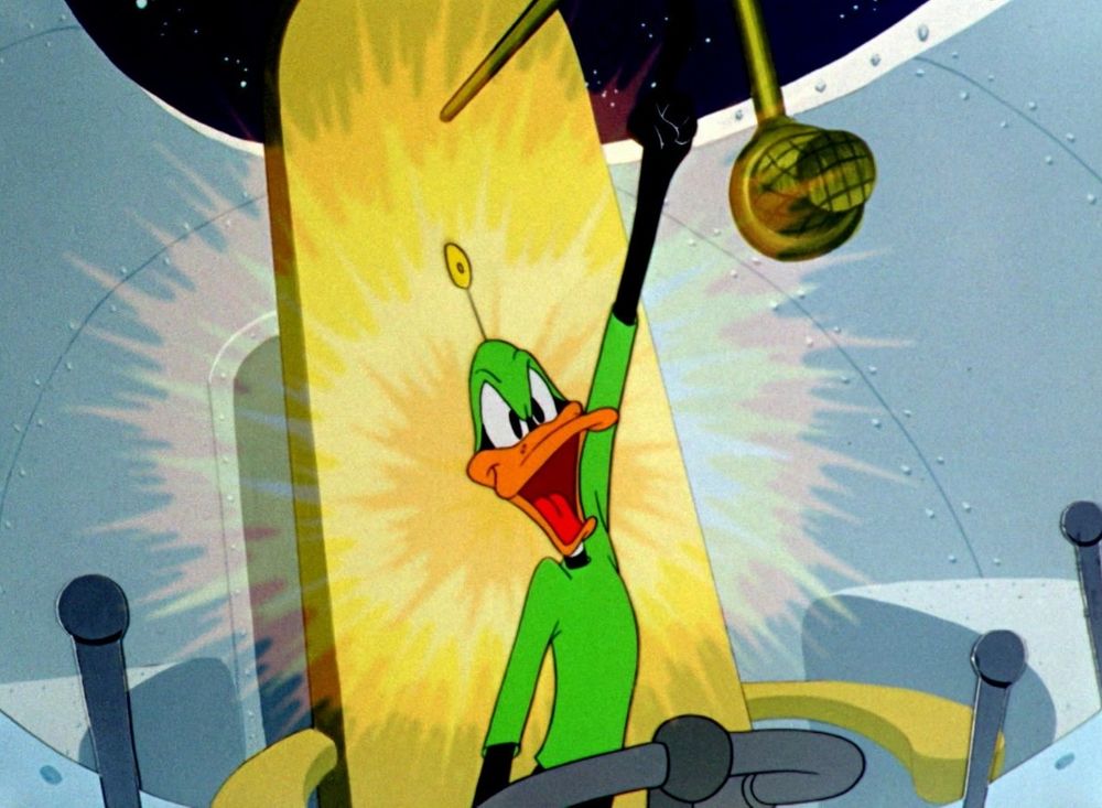 Daffy Duck wearing a space suit sitting in his spaceship "driver's seat" holding his left hand aloft with a sort of explosive aura or halo around him. In the cartoon at this moment, Daffy is saying his character's name valiantly: "Duck Dogers!" 