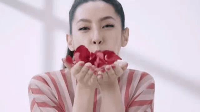 a woman is blowing a kiss with rose petals in her hand .