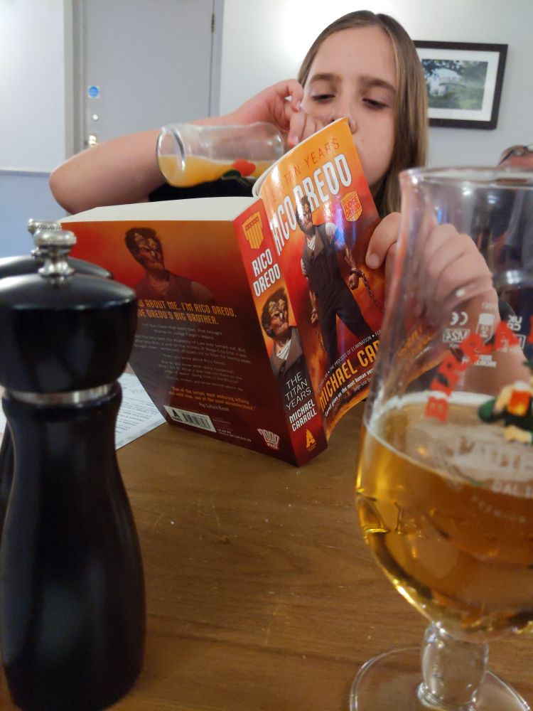 A young reader chugs from a bottle of orange juice whilst avidly devouring 'Rico Dredd: The Titan Years' by Michael Carroll