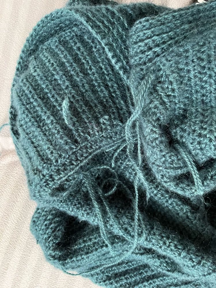 Aufsicht auf ein Durcheinander aus zusammengehäkelten Teilen eines Cardigans mit vielen losen Enden zum vernähen.