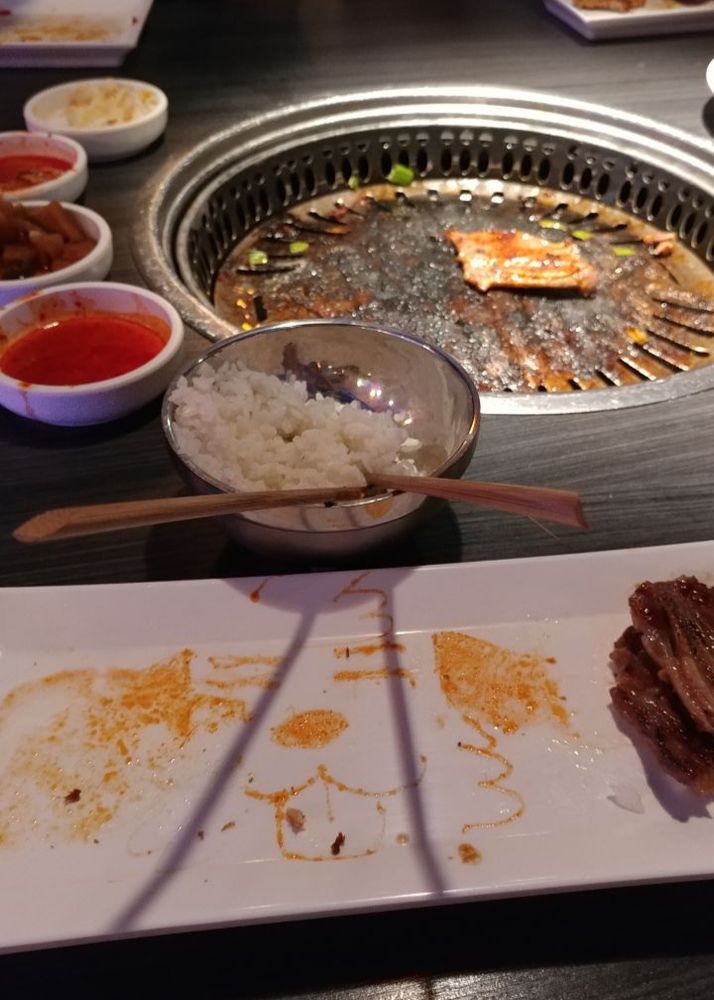 The dog from the previous image is on the plate with some meat, it is partially wiped away from eating on top of it. The KBBQ grill is seen in the background.