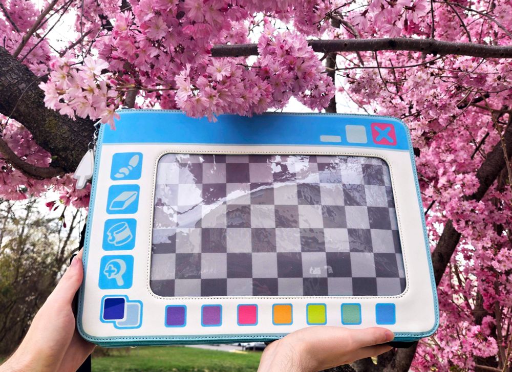 photo of the light mode mx paint laptop bag held up against some blossoms