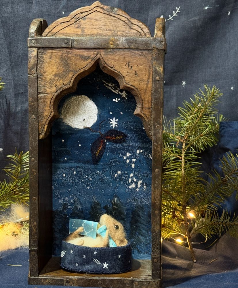 When the spark flies fly wishing stars up to the heavens once again, they are especially powerful so if you look up at the night sky and see one, know that this might just be someone’s thousandth lifetime and their wish will come true. A needle felted dormouse star gazing with their ceramic handmade telescope and star map. They lie in a star embroidered blue linen bed that has an embroidered pillow inside too. The case is a vintage Indian arched box and it is backed with a painting of snowy trees and a night sky. The moon and stars are gilded pure silver. There is a hand embroidered blue linen spark fly with copper antenna flying across the skies. A special piece to remind you to dream and that there is always hope. Inspired from my book The Wish Gatherers