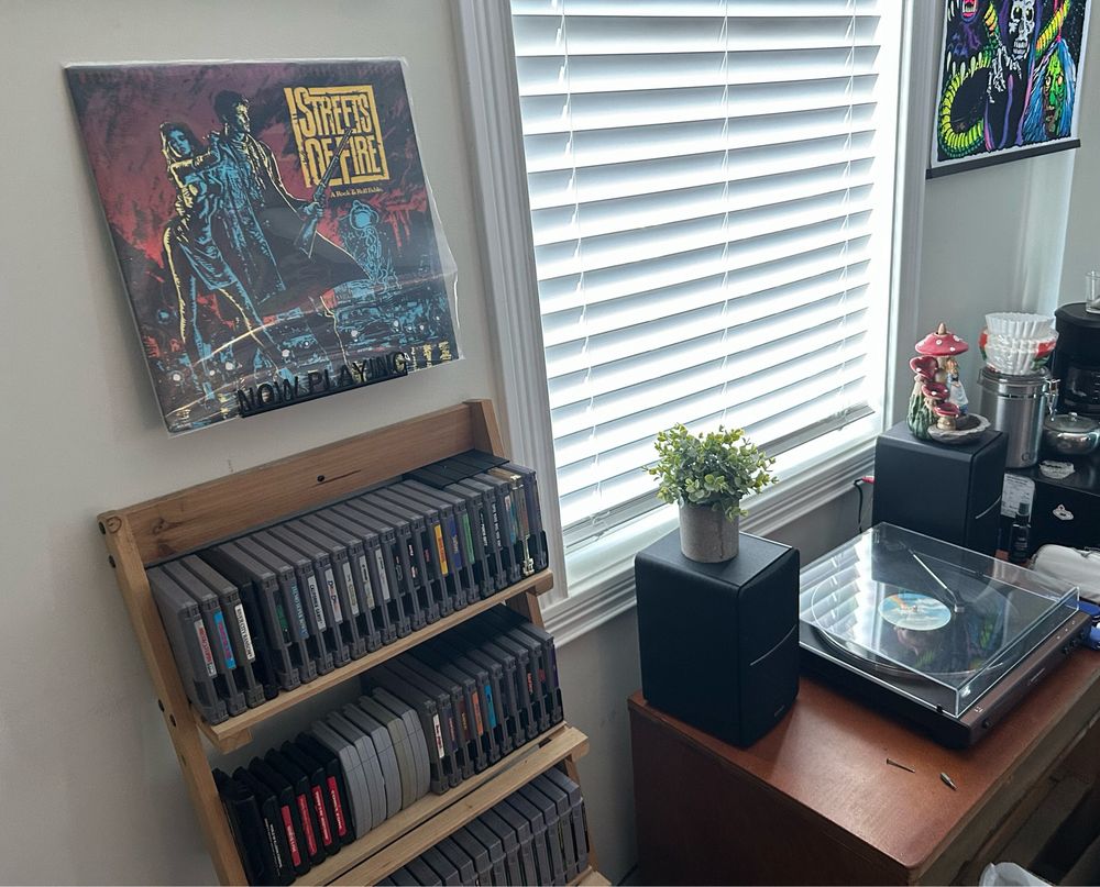 A copy of the Streets of Fire soundtrack on vinyl mounted on the wall beside old game cartridges, the record player playing the album, and a coffee nook in the corner. Meanwhile the morning sun shines in from the window.