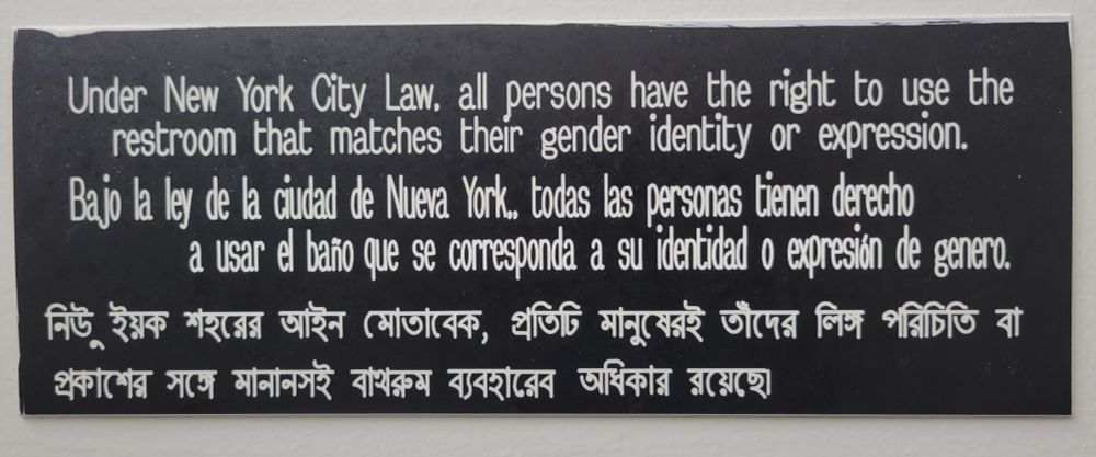 Sign reads "Under New York City Law, all persons have the right to use the restroom that matches their gender identity or expression," in English, Spanish, and Bengali