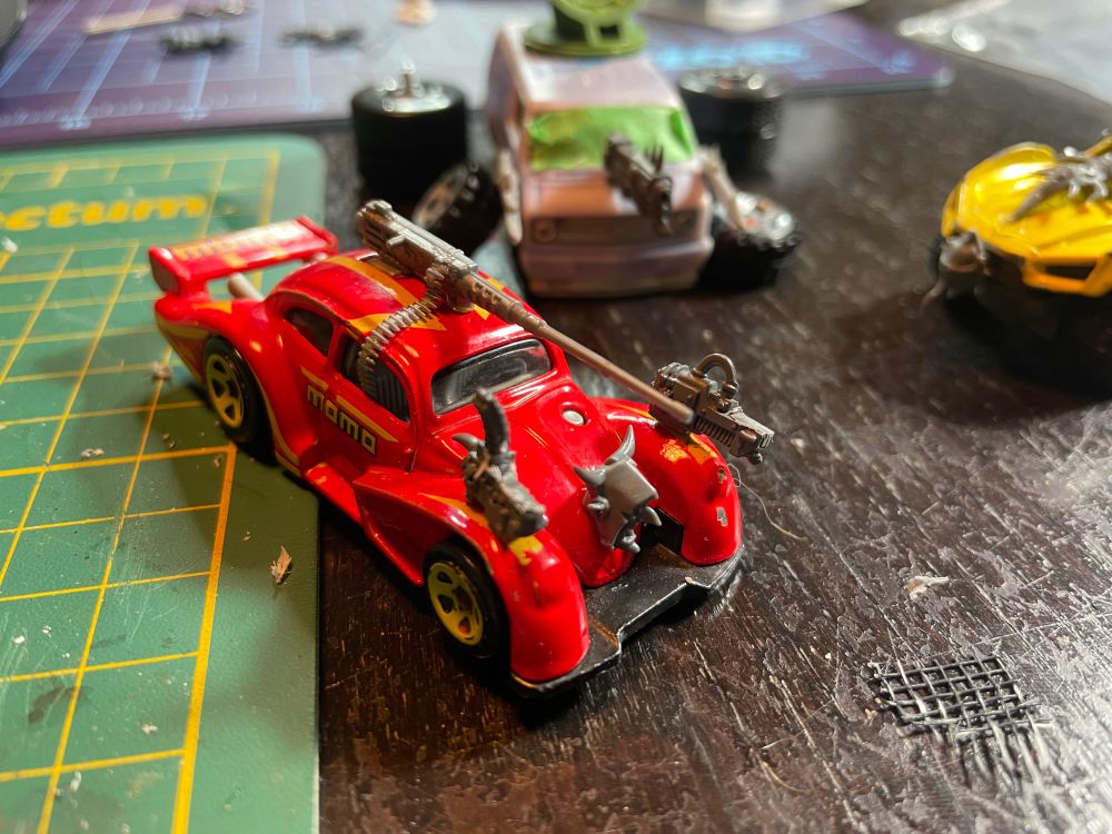 Toy car based on a VW Beetle with a goblin head hood ornament, and a variety of machine guns mounted to it