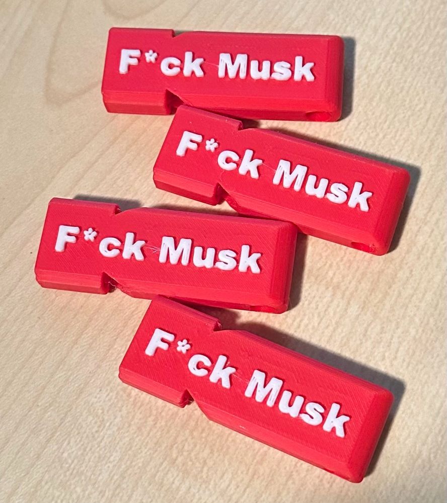 A photograph of four red whistles, on a wooden desktop, with the text “F*ck Musk” in white on each of them.