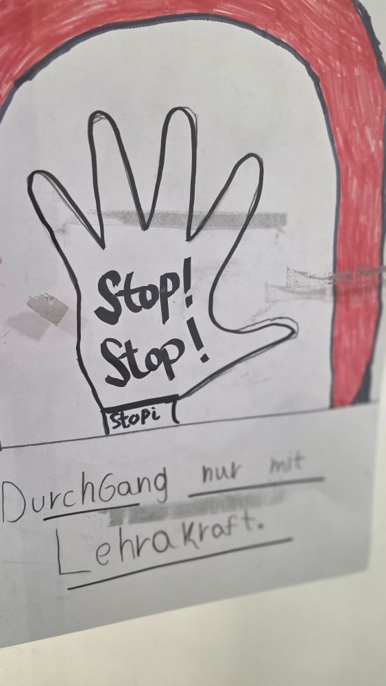 Ein Schild an einer Glastür erstellt von Schülern (m/w/d), drauf eine Hand mit zweimal Stop! Und der Bildunterschrift: "Durchganh nur mit Lehrakraft'.
