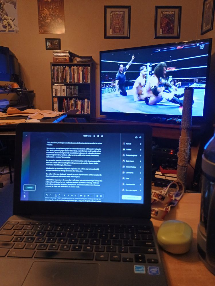 An out of date Chromebook displaying a word processor. In the background is a TV with WWE Main Event playing.