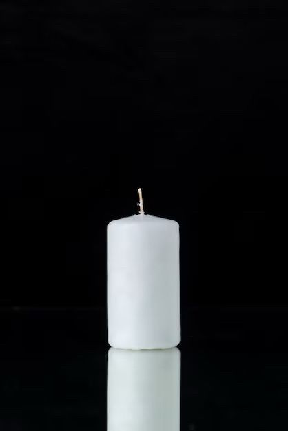 An unlit white candle with a black background.