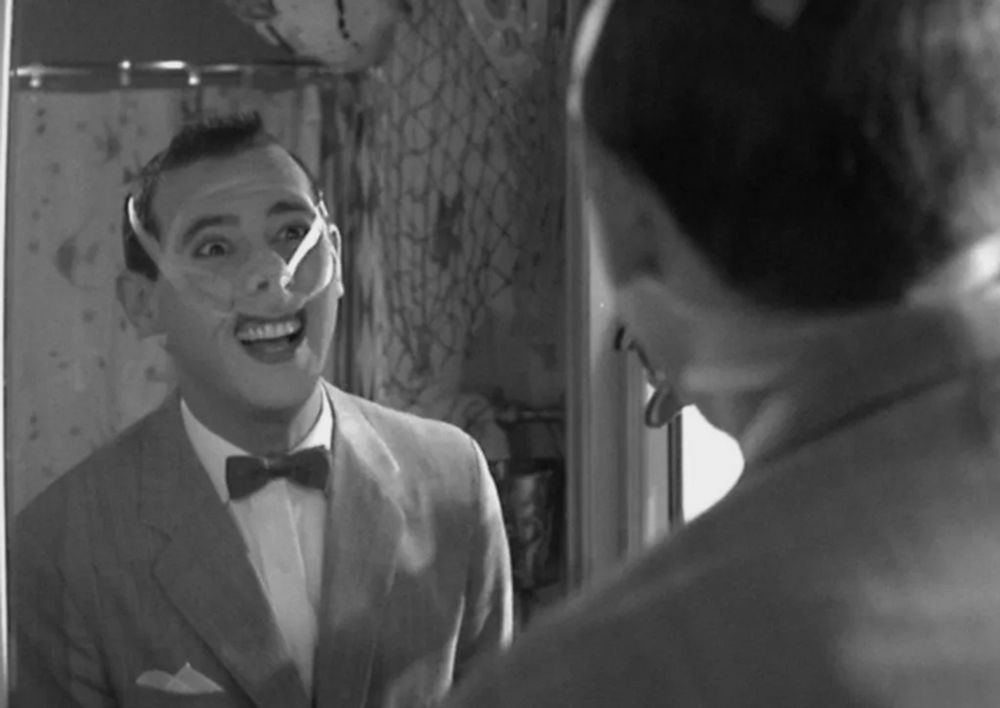 Pee Wee Herman, in black and white, playing with tape all over his face
